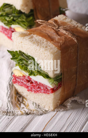 homemade sandwiches with salami and egg wrapped in paper close-up on the table. vertical Stock Photo