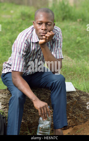 tired young man , sits on a tree trunk very thoughtful. Stock Photo