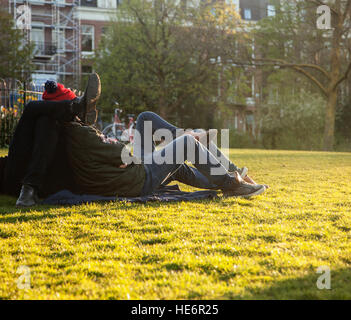 two young guys hipsters chilling on green grass outside in park at sundown, relaxing people lifestyle concept, couple from back Stock Photo