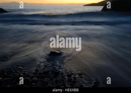 High tide at  a sheltered cove on the Gower Peninsula. A long exposure blurs the  movement of the receding wave Stock Photo