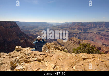 Adventure travel man at edge of the Grand Canyon south rim Pipe Creek Vista taking photo, Arizona USA rear view looking out over majestic Grand Canyon Stock Photo