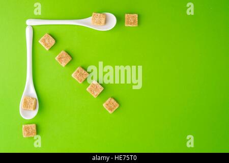 https://l450v.alamy.com/450v/he75t0/brown-sugar-cubes-and-white-spoons-on-greenery-background-arringed-he75t0.jpg