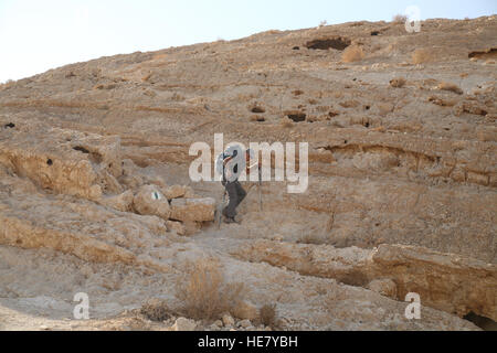 A senior citizen 58 year old man hiker is carefully descending a very steep rocky slope using a hiking stick to avoid falling. Stock Photo