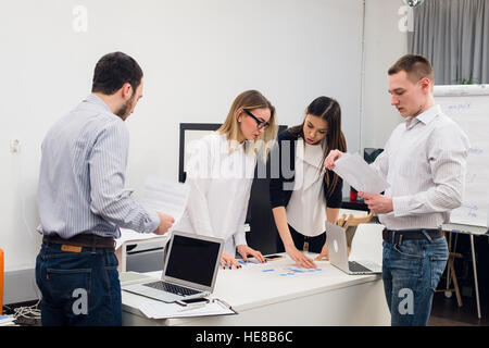 Young business people sitting in office during meeting and discussing with paperwork using laptops Stock Photo