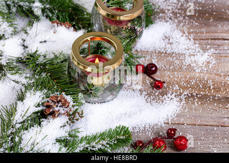 Close up selective focus of burning candle in glass container with snowy fir branches on rustic wood Stock Photo
