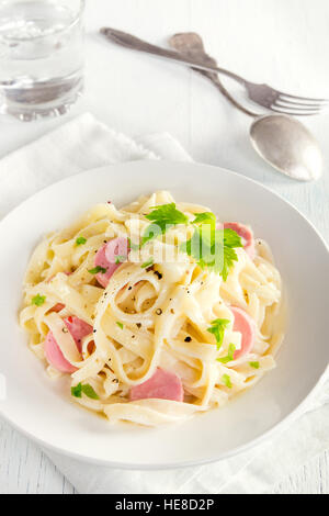 Alfredo tagliatelle pasta with sausages and greens on white plate - homemade creamy pasta Stock Photo