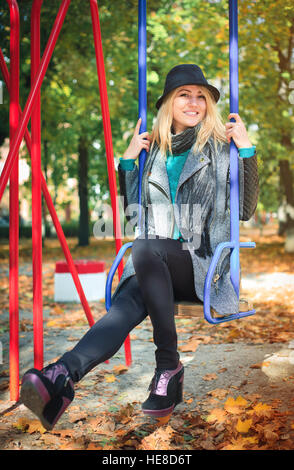 Young beautiful woman on a swing in the park, happy in a sunny autumn day. Stock Photo