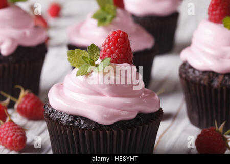 Tasty pastries: chocolate cupcakes with pink cream and raspberry on the table close-up. horizontal Stock Photo