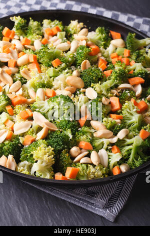 Broccoli with peanuts and carrots close-up on a black plate. vertical Stock Photo