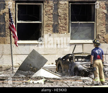 Standing before a burned out hulk of an automobile an Alexandria fireman inspects the damage to the Pentagon. The US flag is set outside the Pentagon after a hijacked American Airlines Flight 77, a Boeing 757-200 was deliberately crashed into Pentagon, September 11, 2001. The Pentagon attack followed an attack on the twin towers of the New York World Trade Center, where two fully loaded passenger airliners were flown into the buildings, in what is called the worst terrorist attack in history. Stock Photo