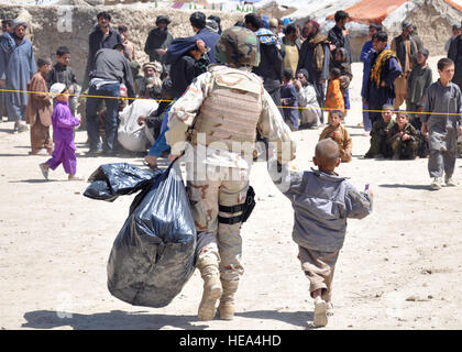 An Albanian army officer assigned to NATO Training Mission-Afghanistan carries a bag of supplies for an Afghan child as she walks him back to his home at a refugee camp in Kabul, Afghanistan, April 18. NTM-A volunteers and Afghan National Police in conjunction with volunteers from Sozo International disseminated supplies such as clothes, flour and toys to refugees. Stock Photo