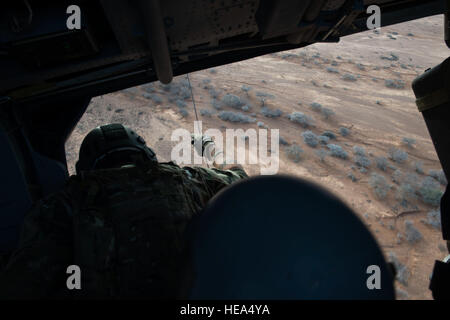 An aerial gunner with the 303rd Expeditionary Rescue Squadron observes and controls deployment of the winch from his position in an HH-60 Pave Hawk during emergency procedures and daytime tactical flight maneuvers training after taking off from Camp Lemonnier, Djibouti, July 10, 2015. The 303rd ERQS conducts training flights to maintain proficiency and provide full mission capability to users while deployed in support of humanitarian aid and contingency operations in the Combined Joint Task Force Horn of Africa area of responsibility. ( Staff Sgt. Gregory Brook/ Released) Stock Photo