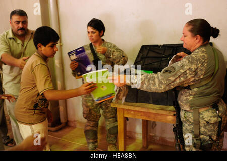 U.S. Army Sgt. Sue Sippel (right) from Union, Mo., from the Public Diplomacy Office, of the Salah ad Din provincial reconstruction team and U.S. Army Sgt. Tessa Smith (center) from Falfurrias,Texas, with Charlie Company, 325th Brigade Support Battalion, 3rd Brigade, 25th Infantry Division, hand out school supplies to local Iraqi children during a site assessment of the Mujamma Youth Center in Mujamma, Iraq, July 9. Stock Photo