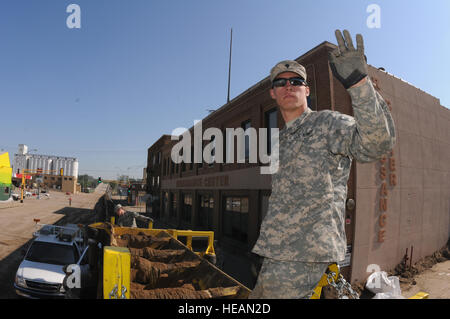 Spc. Lucas Krueger, of the 817th Engineer Company (based in Jamestown, N.D), right, signals heavy equipment operators, June 23, as they load trapbags with sand in Minot, N.D. He is among many North Dakota National Guard soldiers and airmen setting up trapbags in Minot. The trapbags are being set up to act as flood barriers to the rising Souris River. The trapbag barrier is a secondary level of protection, which will allow some roads to remain open once the water exceeds the first level of flood levees in the coming days. The flood water is already over-topping the primary flood levees in some  Stock Photo