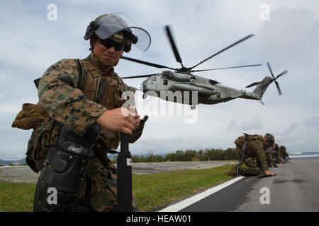 Cpl. Jordan Canchola, an artillery gunner with Golf Battery, Battalion Landing Team 1st Battalion, 5th Marines, 31st Marine Expeditionary Unit, takes a knee to shield himself from the rotor wash of a CH-53E Super Stallion helicopter at Camp Courtney in Okinawa, Japan, Dec. 15, 2015. The battery was training to distribute food and water as part of a humanitarian assistance and disaster relief operation when the crowd, played by other Marines, became unruly. A quick reaction force was called to help restore order and continue to distribute supplies. The HADR training was conducted as part of the Stock Photo