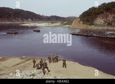 A partially completed pontoon bridge built by the 50th Engineers, 1st Platoon, Camp Laguardia, Republic of Korea, (ROK), ferries two M2 Bradley Fighting Vehicles assigned to the 2-9 Infantry, Camp Casey,  (ROK),  during a bridge building exercise and simulated crossing of the Imjin River, ROK,  on Oct. 22, 1998. The bridge if completed would begin where the soldiers are standing in the foreground, and end just at the base of the hill directly across the river from them. Many of the participants in today's exercise are officers participating in accordance with the U.S. Army Officer Professional Stock Photo