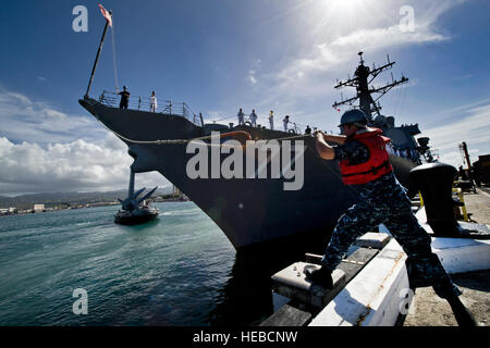 U.S. Navy Petty Officer 2nd Class Joshua Thomas casts a mooring line to sailors aboard the guided-missile destroyer USS O'Kane (DDG77) as it departs Joint Base Pearl Harbor-Hickam, Hawaii, March 23, 2012, for a deployment to the Western Pacific. USS O'Kane, is deploying under the Middle Pacific Surface Combatant deployment concept in which Pearl Harbor-based ships deploy in support of operations primarily in the Western Pacific under Commander, U.S. 7th Fleet. Stock Photo