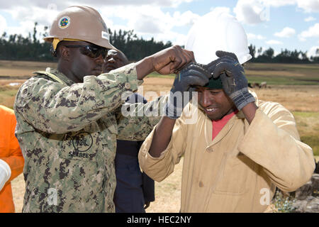 U.S. Navy Petty Officer 2nd Class Orlando Moore, U.S. Naval Mobile Construction Battalion 1 equipment operator, provides personal protective equipment to Ethiopian National Defense Force Pvt. Negero Turi Jaleta, engineer, before drilling operations commence in Fiche, Ethiopia, Dec. 17, 2012. NMCB 1 Seabees attached to Combined Joint Task Force-Horn of Africa partnered with ENDF engineers during a water well drilling exercise beginning Nov. 27, 2012. The exercise strengthened the operational and institutional capabilities of the ENDF and helped build the relationship between the two militaries. Stock Photo