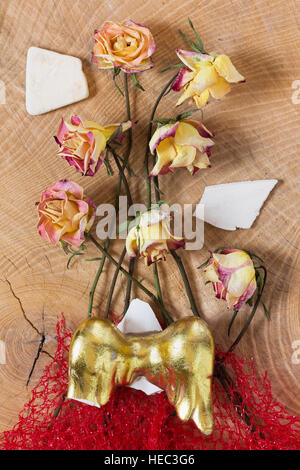 Withered faded sad roses, red net and golden broken angel wings on wooden background as studio close up, symbolic fantasy image Stock Photo