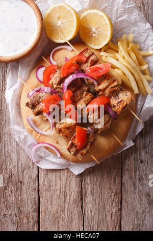 Greek souvlaki kebabs with vegetables and french fries on pita bread on the table. vertical top view Stock Photo