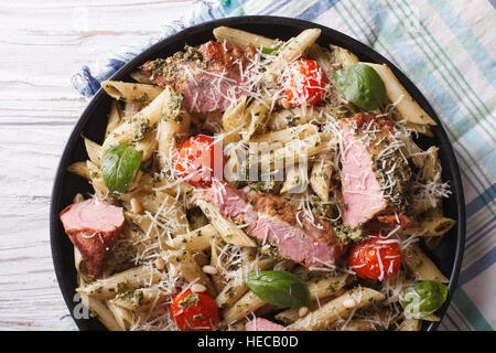 Italian pasta penne with meat, parmesan cheese, tomato and pesto sauce on a plate close-up. horizontal view from above Stock Photo