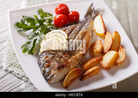 Grilled dorado fish with fried potatoes and lemon on a plate close-up. Horizontal Stock Photo