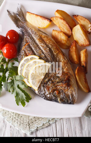 Grilled dorado fish with fried potatoes and lemon on a plate close-up. vertical Stock Photo