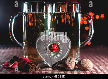 Funny image of two beer glasses of champagne, decorative heart, cinnamon and walnuts on the background of lights bokeh. Low key. Stock Photo