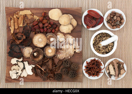 Traditional chinese herb selection used in herbal medicine on maple wood board and in porcelain bowls with mortar and pestle on bamboo. Stock Photo