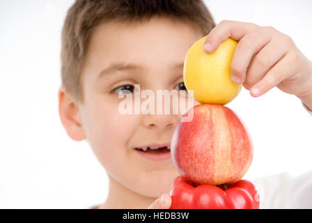 7-year-old boy stacking a pepper, an apple and a lemon Stock Photo