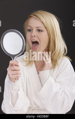 Woman looking into the mirrow, sticking out her tongue Stock Photo