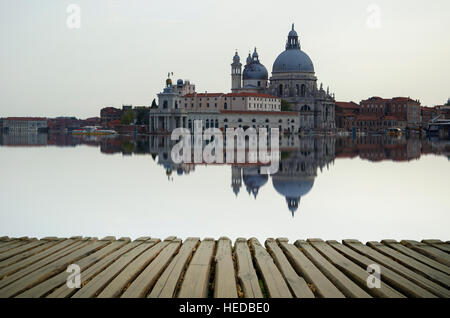 Fine art image with Grand Canal and Basilica Santa Maria della Salute, reflected on the water surface, with wood planks floor fo Stock Photo