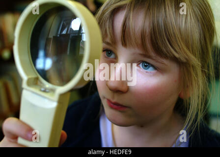 A primary aged schoolgirl peering through a large magnifying glass.a UK school education science Stock Photo