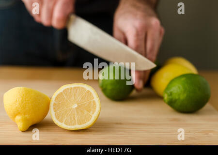 A man's hands slicing lemons and limes on a cutting board with a chef's knife. Stock Photo