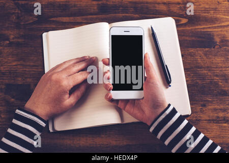 Top view mock up of businesswoman hands using smartphone on office desktop with notebook in background, retro toned Stock Photo