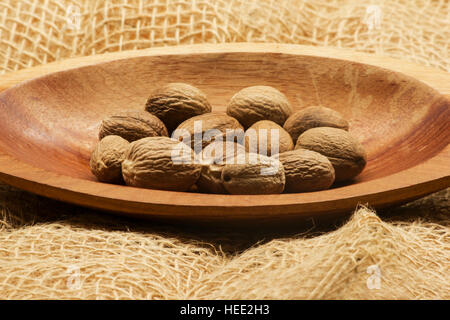 Nutmegs (Myristica fragrans) in a wooden bowl on burlap Stock Photo