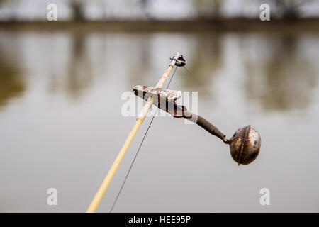 The bell on the top of fishing rod in front of water surface. Old spinning equipment. Selective focus, shallow DOF. Stock Photo