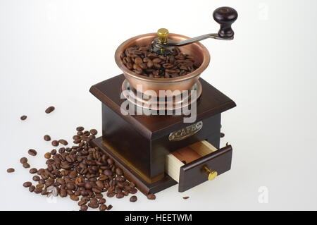 Old-style manual coffee grinder on the white background. Around the mill are scattered coffee beans. Stock Photo