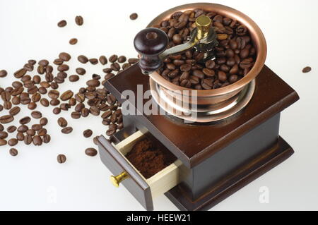 Old-style manual coffee grinder on the white background. Around the mill are scattered coffee beans. Stock Photo