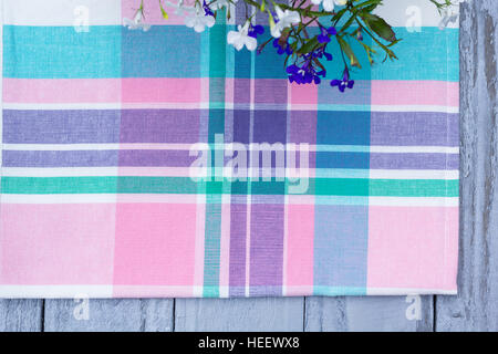 Close up on checkered tablecloth fabric. pink, green, violet with white tartan square pattern with blooming lobelia flowers Stock Photo