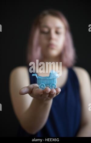 A teen girl holding a miniature baby carriage in the palm of her hand. Stock Photo