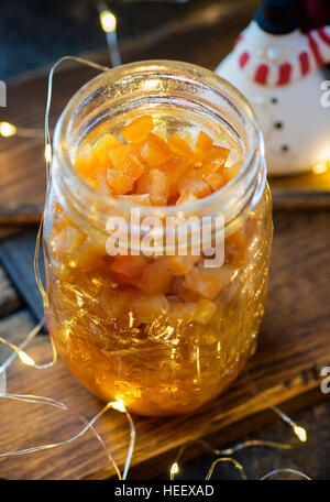 Homemade candied orange peel in glass jar over dark background, festive lights on back, selective focus, Christmas baking ingredient Stock Photo