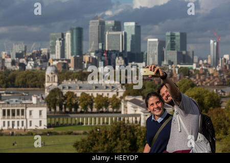 A couple taking a selfie from the Greenwich Park viewpoint overlooking the Old Royal Naval College and Canary Wharf, London, UK. Stock Photo