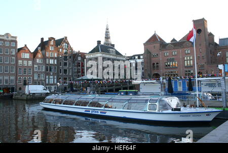 Canal cruise boat moored at Damrak waterway, Amsterdam, Netherlands. Beurs van Berlage in background Stock Photo