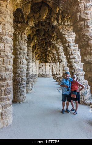 Two tourists, a man and his wife, walk along a line of stone arches in Park Grüell designed by Gaudí in Barcelona, Spain. Stock Photo