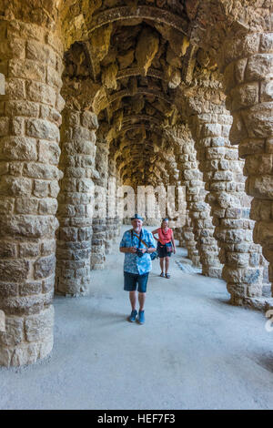 Two tourists, a man and his wife, walk along a line of stone arches in Park Grüell designed by Gaudí in Barcelona, Spain. Stock Photo