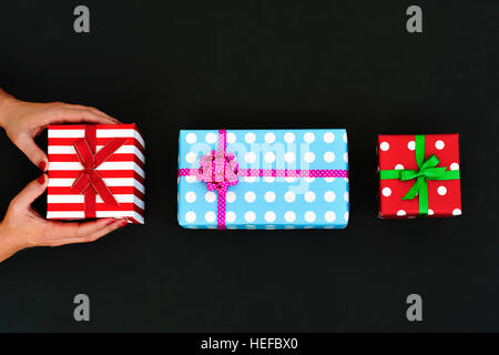 high-angle shot of a young caucasian woman with some gifts arranged in line on a dark gray surface, and wrapped in colorful papers and tied with ribbo Stock Photo