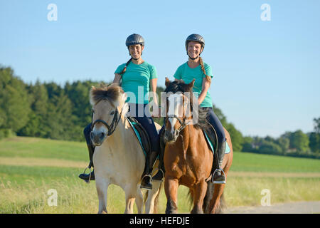 Two girls riding hand in hand on back of a Norwegian Fjord horse and an Irish Cob horse Stock Photo