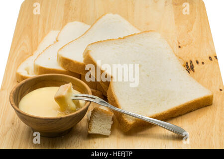 Portion of bread dip in sweetened condensed milk on wooden board Stock Photo