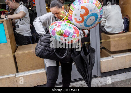 Woman trying to find something her handbag whilst keeping hold of helium balloons Stock Photo